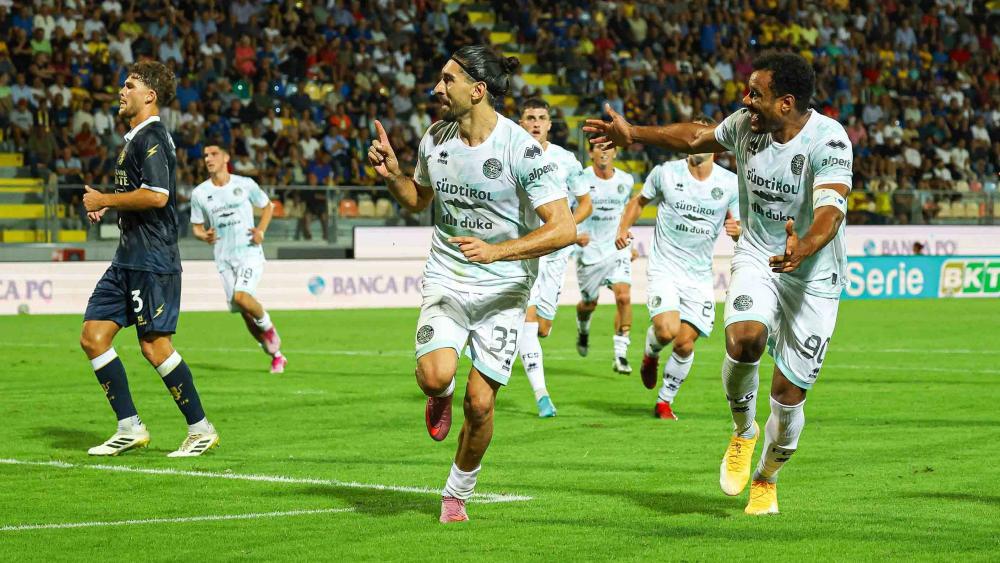 FCS-Held Silvio Merkaj (links) wird von Raphael Odogwu und den weiteren Mitspielern gefeiert. © FC Südtirol