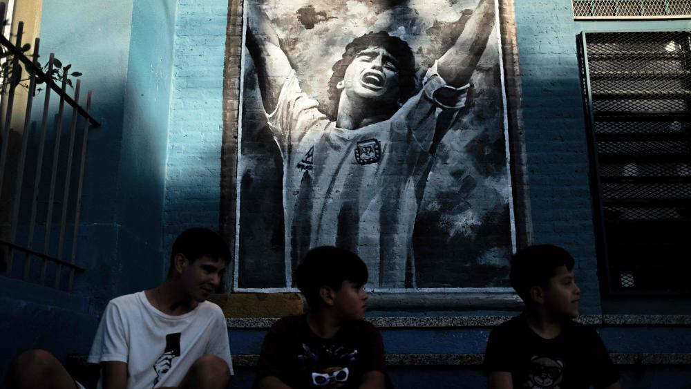 Kinder sitzen vor einem Maradona-Gemälde: Der Argentinier ist auch nach seinem Tod allgegenwärtig. © APA/afp / TOMAS CUESTA
