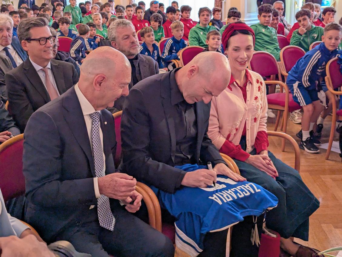 Zinedine Zidane signiert ein Obermais-Trikot, das der Verein Vizebürgermeister Nerio Zaccharia (l.) überreicht hatte.